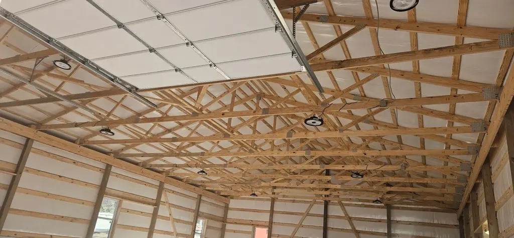 High-bay LED lighting installed in a pole barn ceiling with exposed wood trusses